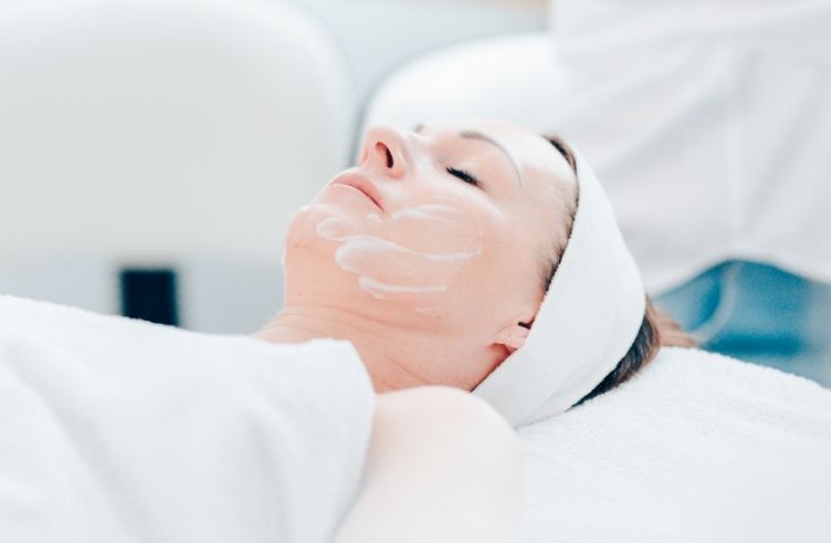 Dame bei einer Schönheitsbehandlung gegen Akne mit aufgetragenem Pflegeprodukt auf dem Gesicht 